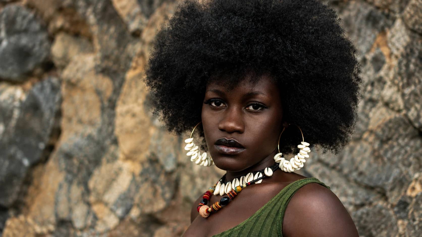 Portrait d’une femme avec une coiffure afro volumineuse et des boucles d’oreilles en cauris